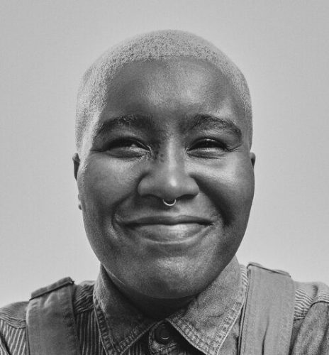 Queer Black Nigerian-American non binary author Candice Iloh smiling. They have dark skin tone and short blonde hair.