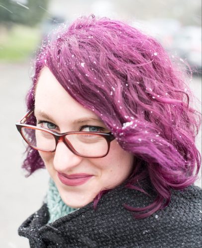 Queer author Rosiee Thor is a woman with purple hair, light skin tone, blue eyes, and glasses.