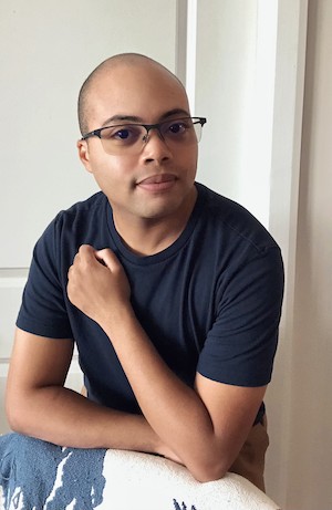 Queer author Isaac Fitzimmons with short dark hair and facial hair, medium skin tone, brown eyes, and glasses.