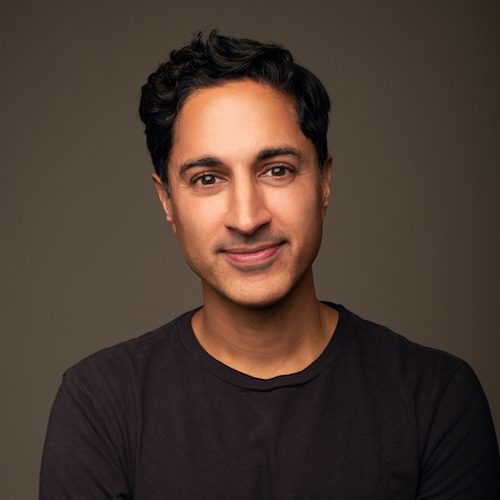 Actor/Writer Maulik Paucholy has medium skin tones and dark short hair. He is wearing a black shirt and is smiling at the camera.