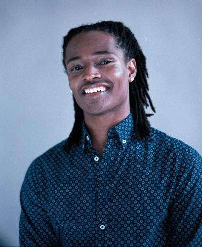 Black male author smiling in a collared shirt and small pearl earrings.